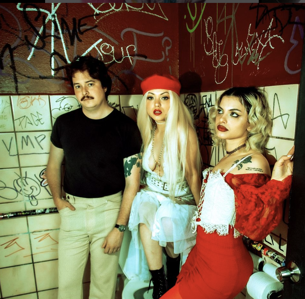 Casey, Rena, and Nia stand in front of graffiti bathroom walls.